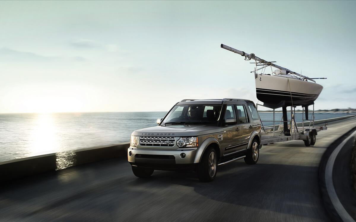 Land rover discovery 4 едет по берегу моря с прицепом с лодкой