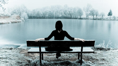 A girl on a bench by a frozen lake