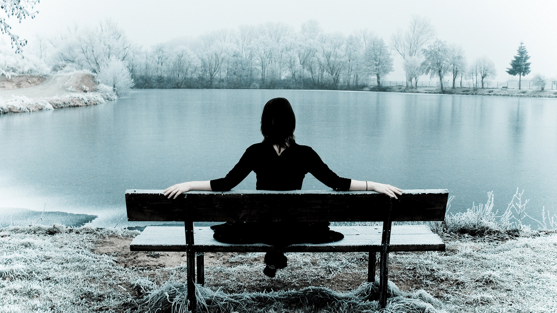 免费照片一个女孩坐在冰湖边的长椅上。