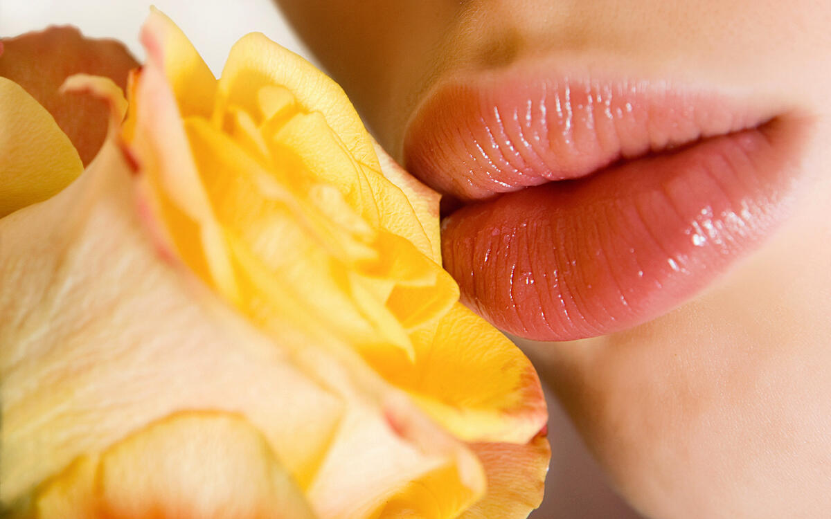 A woman`s lips next to a yellow rosebud.