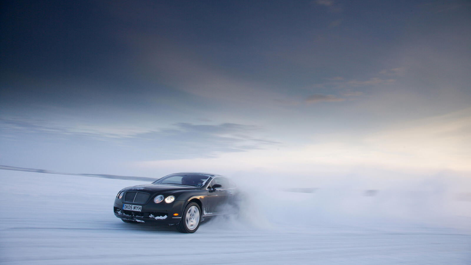 Free photo A black Bentley drifting across a snowy field.