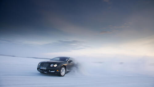 A black Bentley drifting across a snowy field.
