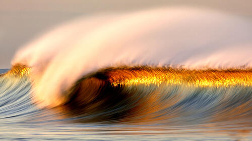 A large wave changes color from sunlight