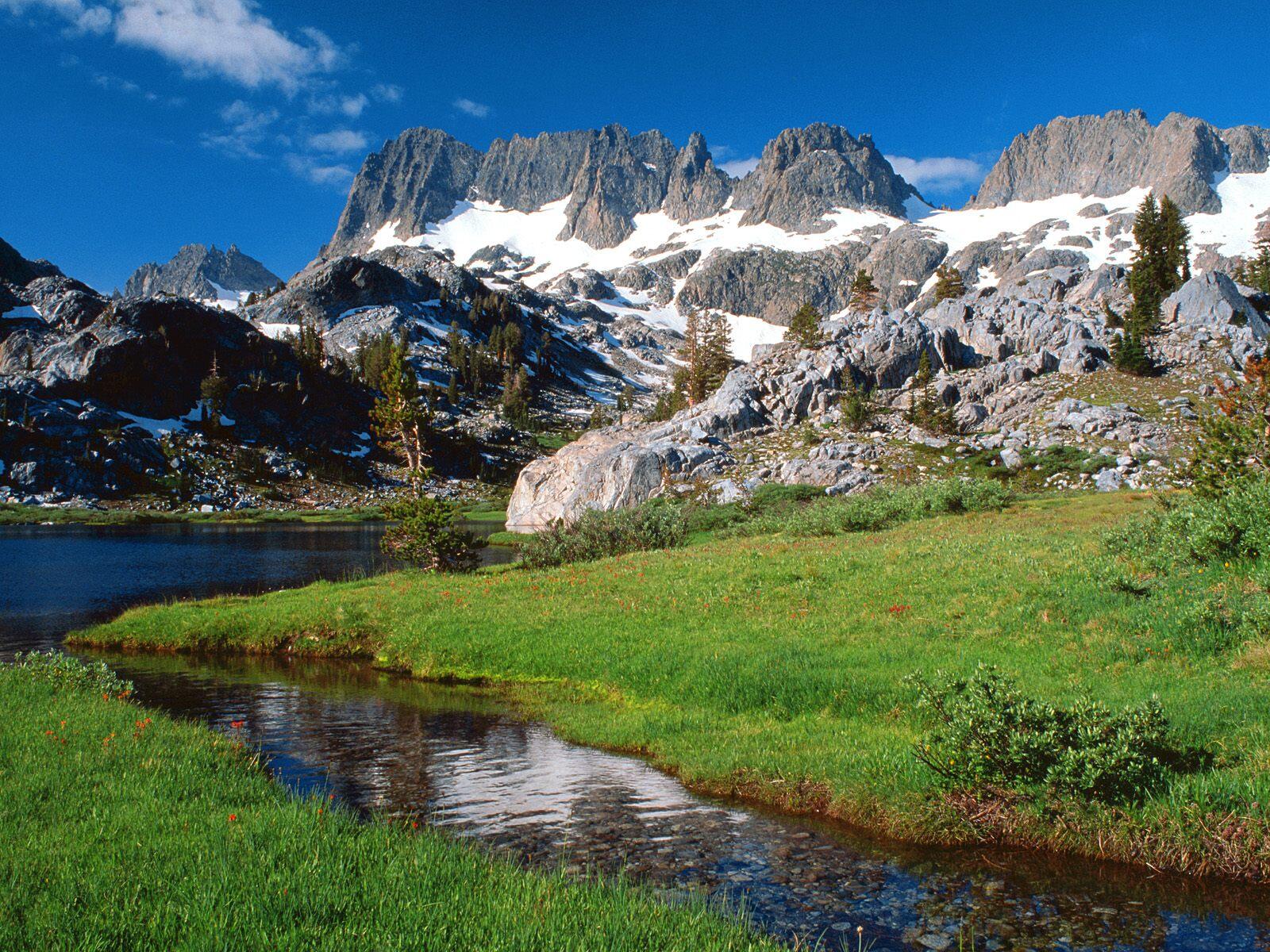 Бесплатное фото Зеленая полянка рядом с горами покрытыми снегом