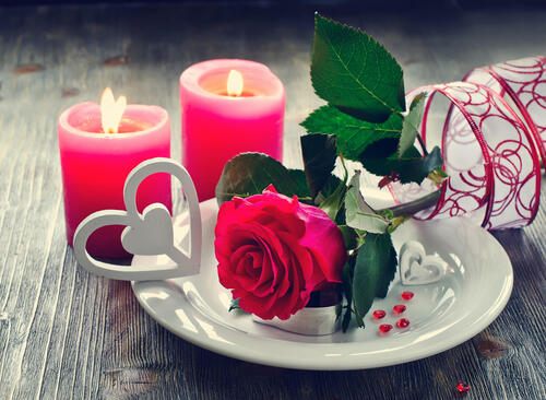 A red rose lies in a plate next to burning candles