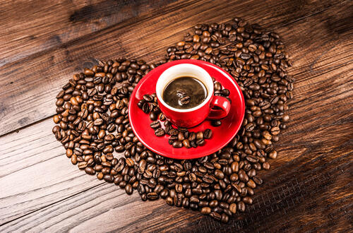 Кофейные зерна уложенные в виде сердца с красной чашкой кофе