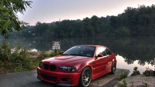 A red bmw m3 is parked by the river.
